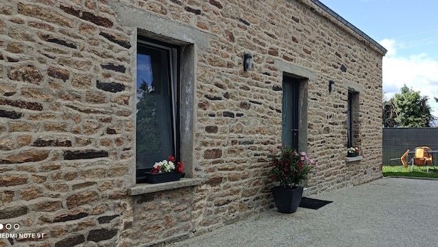 Un edificio de piedra con dos ventanas, una puerta y un pequeño espacio al aire libre con sillas y una mesa.