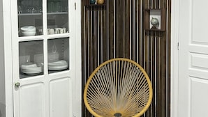Una habitación de esquina con un armario blanco, una silla de mimbre y un panel de pared de madera.