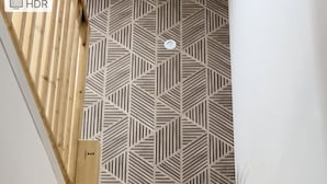 Una escalera de madera con un muro de diseño geométrico y una maceta blanca con plantas en la parte superior.