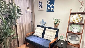 A cozy living room with a blue sofa, a wooden side table, a potted plant, and a wall-mounted shelf with decorative plates. - Tabi Time Oimazatominami (Osaka)