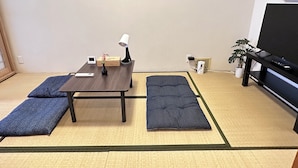 A room with tatami mats, a low table with a lamp, a remote control, a small clock, and a potted plant. - Tabi Time Oimazatominami (Osaka)