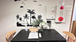 A room with a black table, two wooden chairs, a wall-mounted fire alarm, a wall decal of palm trees, and a vase with flowers. - Tabi Time Oimazatominami (Osaka)