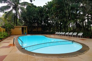 Ein Pool mit gewölbter Kante, umgeben von Palmen und einem kleinen Gebäude.