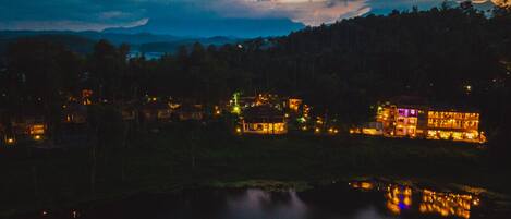 A lakeside view of a resort with multiple buildings, including a large resort building and smaller cabins, surrounded by dense forest.
