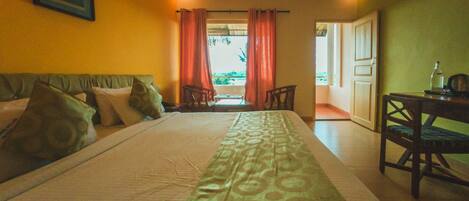 Habitación de hotel con una cama grande, un escritorio con una silla y vistas al exterior a través de una puerta.