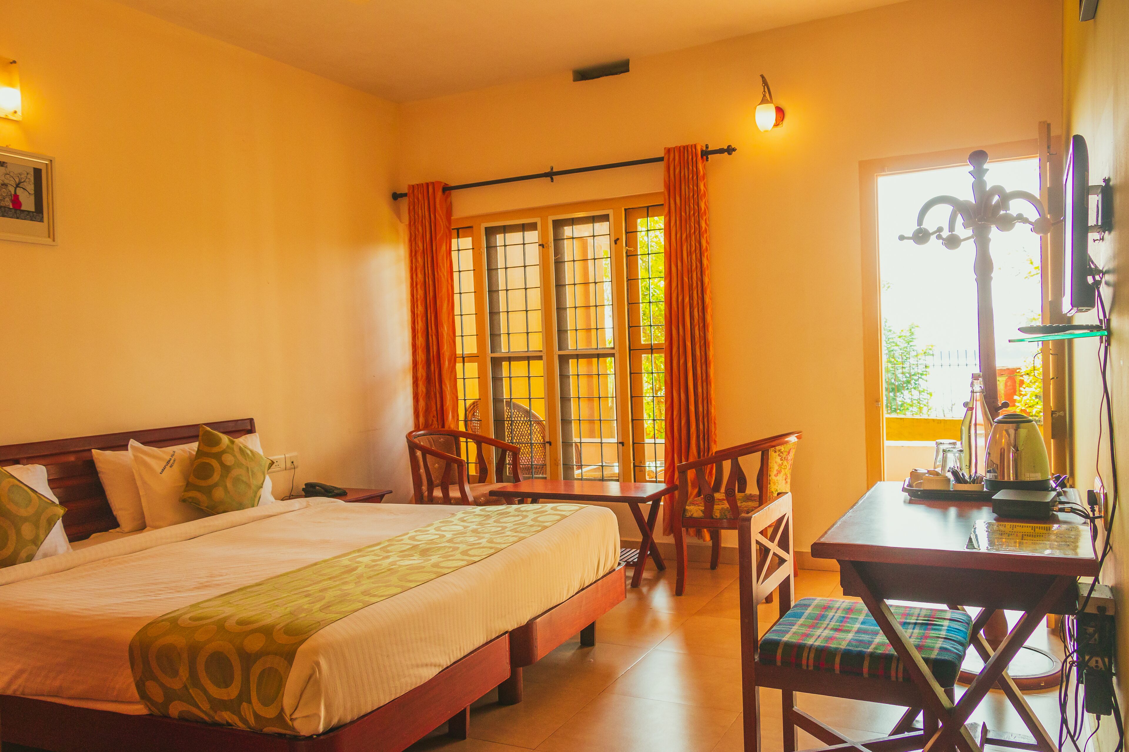 A hotel room with a bed, a desk, and a chair. There is a window with curtains, a picture on the wall, and a lamp on the desk.