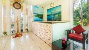 Uma área de recepção com um relógio, um cartaz emoldurado, uma cadeira vermelha e uma mesa de vidro com uma flor.