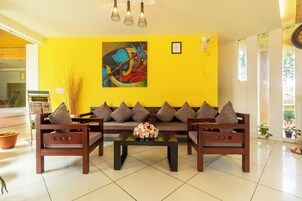 Una sala moderna con una pared de acento amarilla, un conjunto de sofá, una mesa de centro con flores y un cuadro.