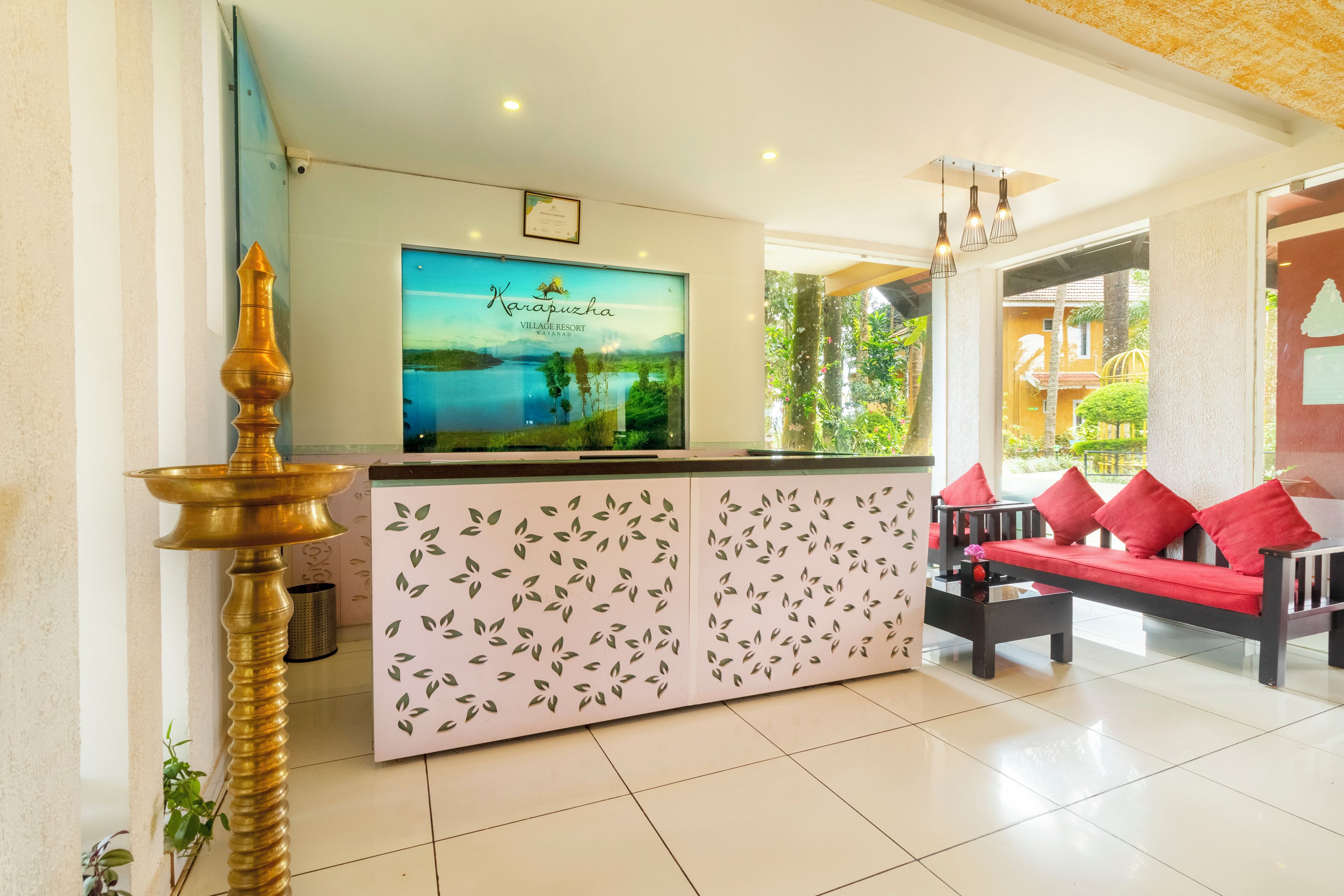 A reception area with a large TV screen, a decorative lamp, a sofa with red cushions, and a patterned cabinet.