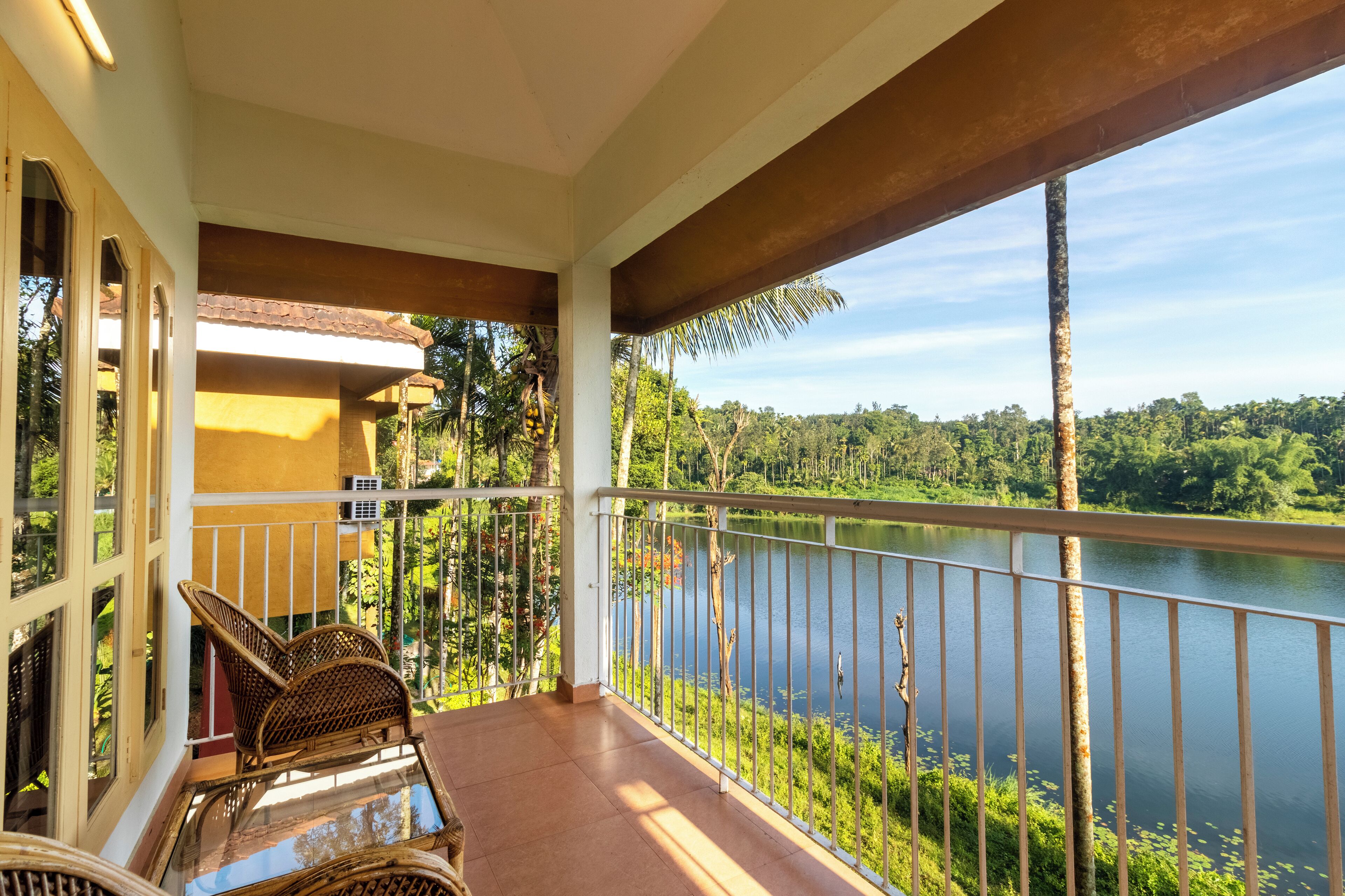 A balcony with wicker furniture, a view of a lake, and a forested landscape.