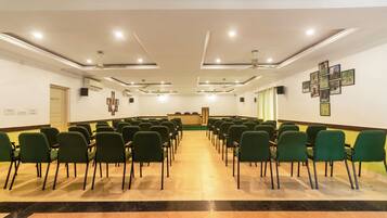 A conference room with rows of green chairs, a podium, and a ceiling with recessed lighting and a fan.