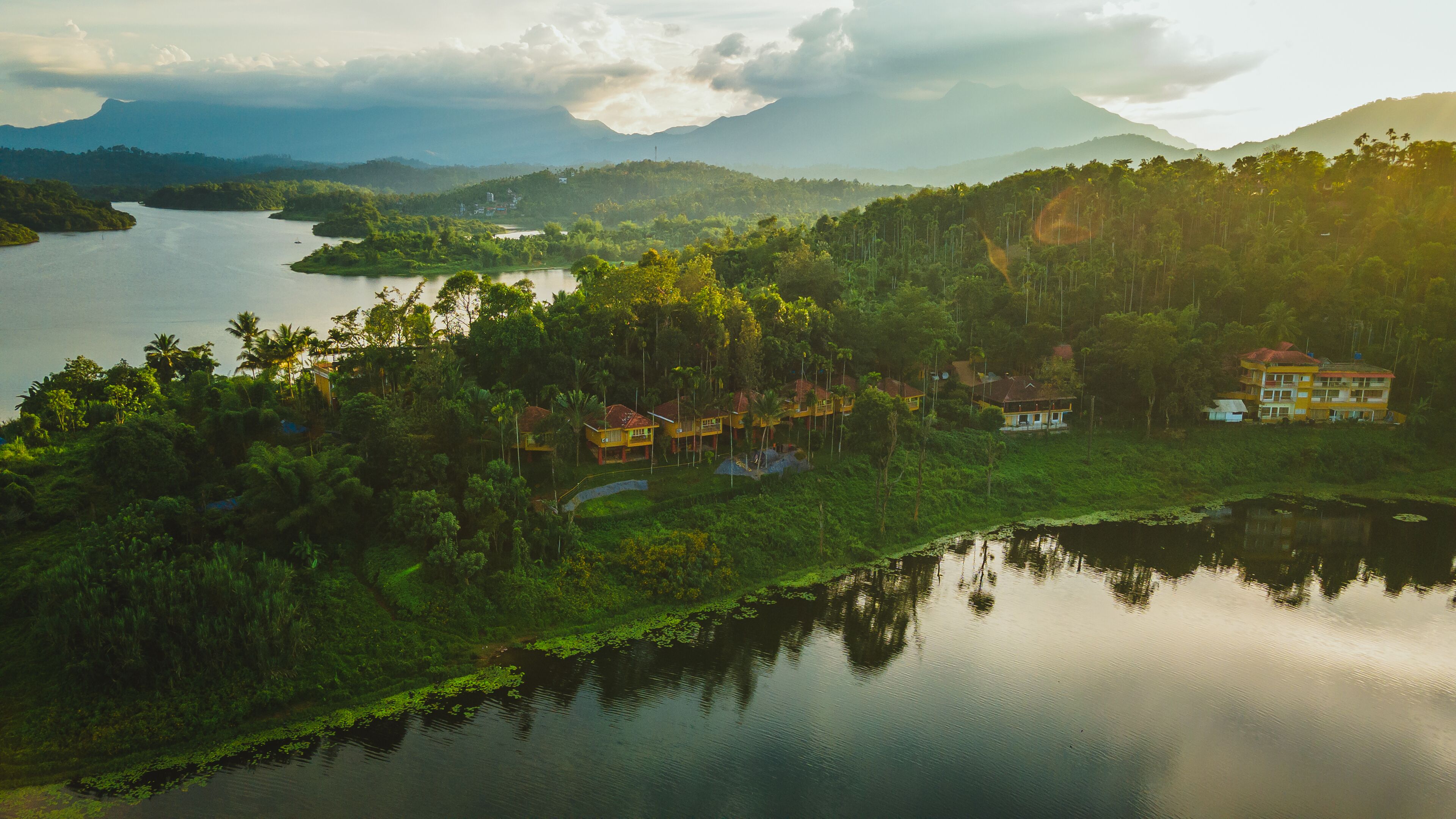 A tropical resort with multiple bungalow-style buildings surrounded by lush greenery and a calm lake.