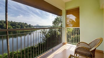 Un balcón con vistas a un lago y un bosque, una silla de mimbre y una ventana con persiana de bambú.