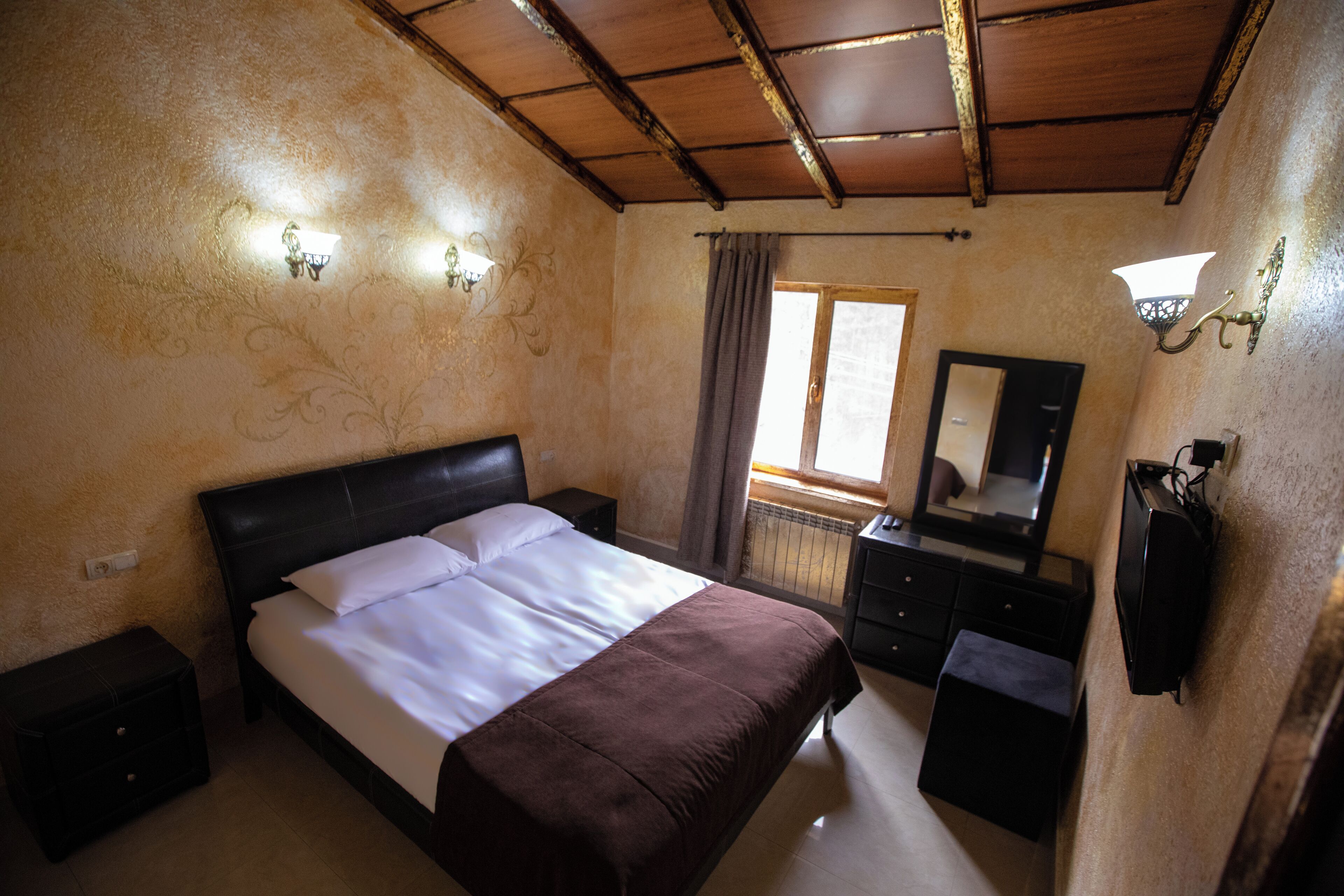 A bedroom with a bed, a dresser, a nightstand, a mirror, and a window with curtains.