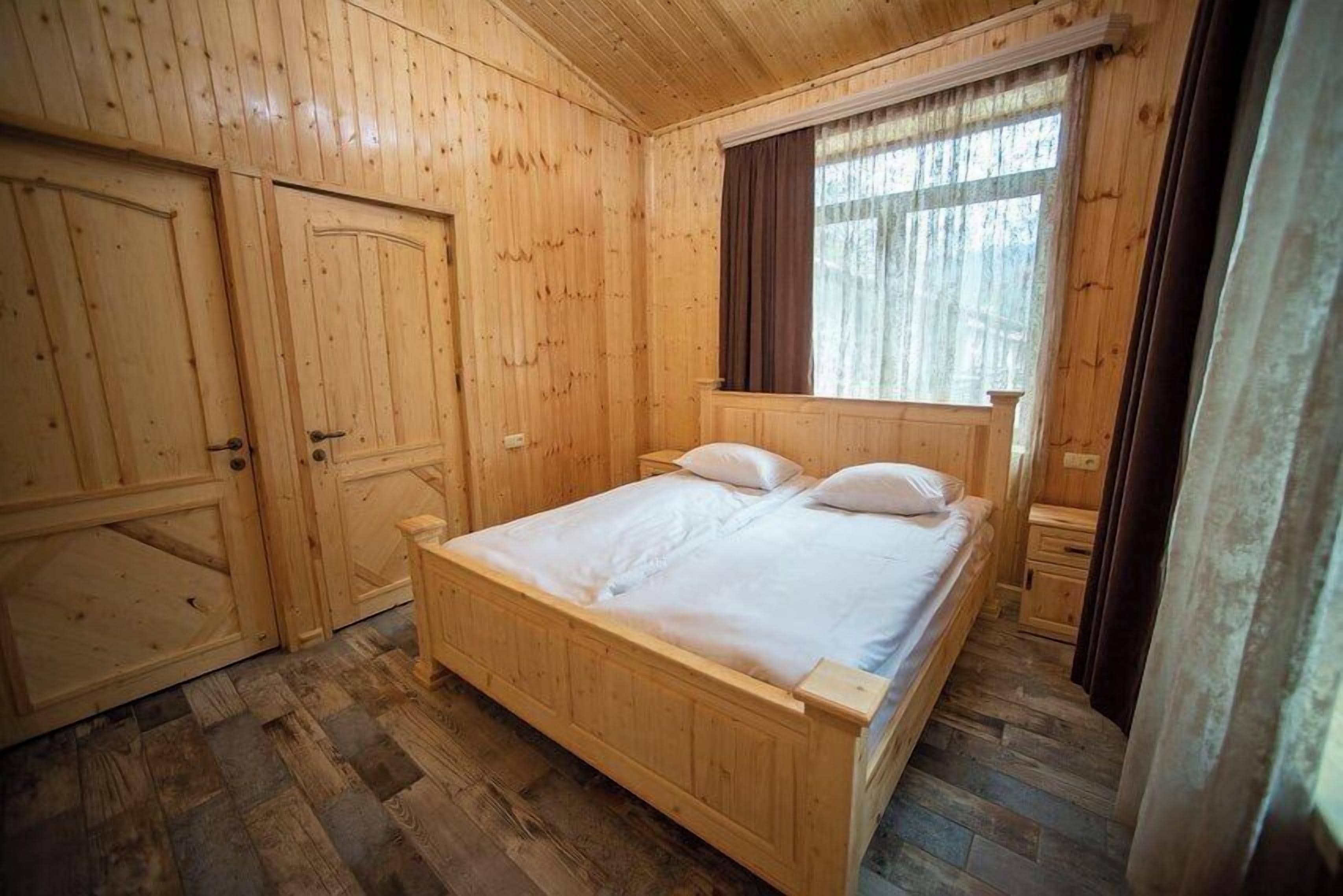 A wooden room with a bed, a wardrobe, and a window with curtains.