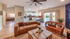 A spacious living room with a brown leather sofa, a wooden coffee table, and a ceiling fan. - Hacienda San Miguel | Resort Style Pool W/ Sunken Outdoor Kitchen (Indio)