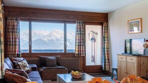 A cozy living room with a sofa, a coffee table, and a view of mountains through large windows. - Magrappé 344 by Interhome (Veysonnaz)