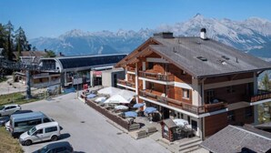 A mountain lodge with a wooden facade, a balcony with outdoor seating, and a view of snow-capped peaks in the background. - Magrappé 344 by Interhome (Veysonnaz)