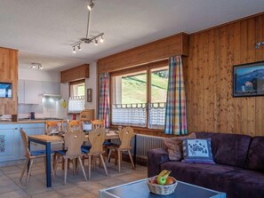 Ein gemütliches Zimmer mit einem Holzesstisch, Stühlen, einem violetten Sofa und einem Fenster mit Vorhängen.