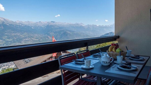 A table set with a basket of fruit, a teapot, and cups, overlooking a mountainous landscape. - Magrappé 344 by Interhome (Veysonnaz)