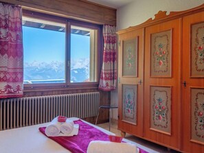 Ein Hotelzimmer mit einem Bett, einem Fenster mit Vorhängen, einem Heizkörper und einem Holzschrank mit Verzierungen.