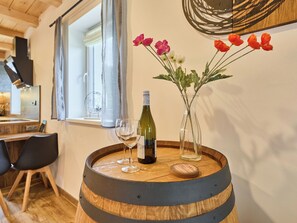 Una mesa de madera con barriles, una botella de vino, dos copas de vino y un florero con flores.