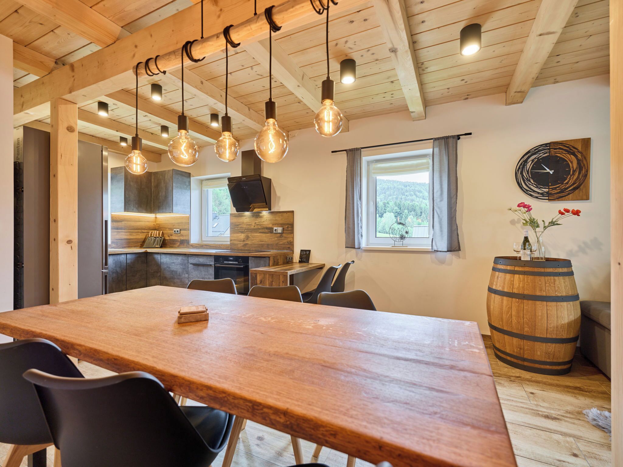 Un coin repas avec une table et des chaises en bois, une cuisine en arrière-plan et un tonneau en bois.
