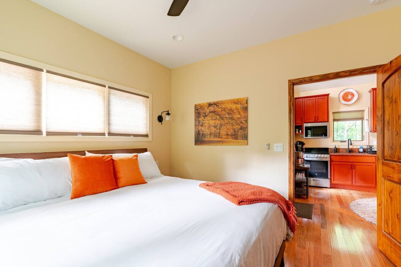 Ein Schlafzimmer mit einem Bett, einem Gemälde und Blick in eine Küche mit Holzschränken und Geräten.