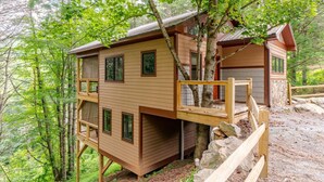 A two-story wooden cabin with a balcony, surrounded by trees. - Spring in Mtns Poplar Treehouse Near Asheville - Pet Friendly (Marshall)