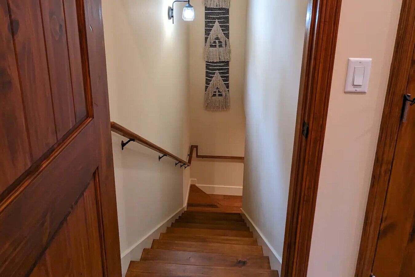 A wooden staircase with a handrail, a wall-mounted light fixture, and a hanging wall decoration.