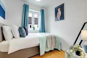 Ein Schlafzimmer mit einem Bett, Vorhängen, einem Fenster, einer Pflanze und einem Poster an der Wand.