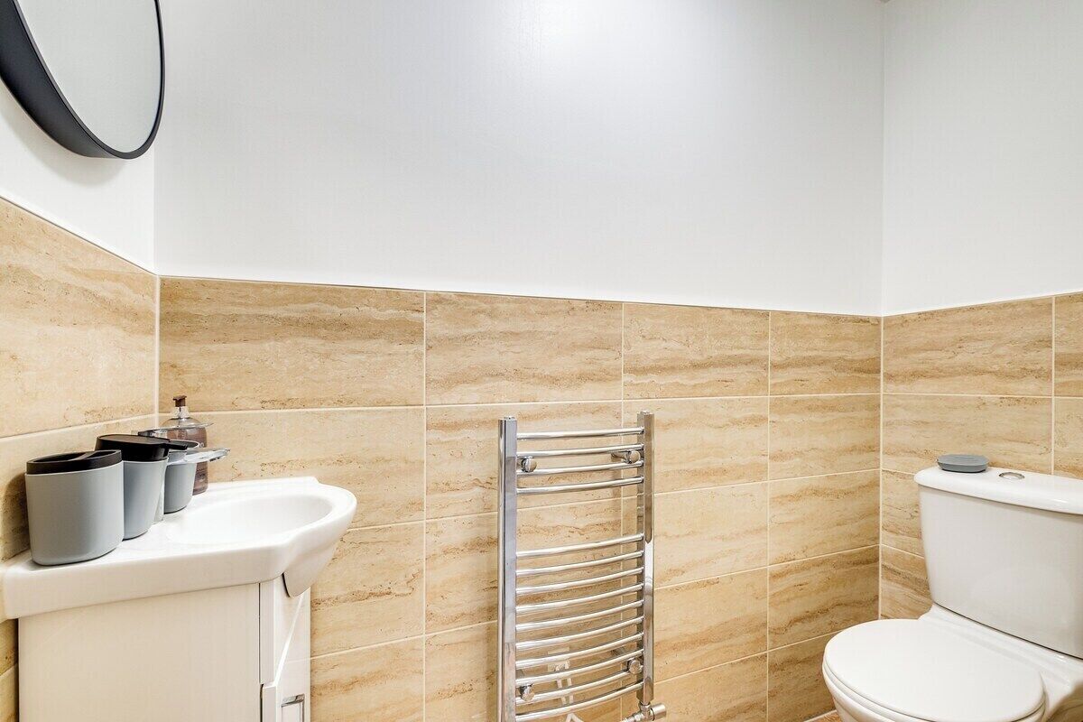 Ein Badezimmer mit beigen Fliesen, einem weißen Waschbecken, einem chromfarbenen Handtuchhalter und einer Toilette.
