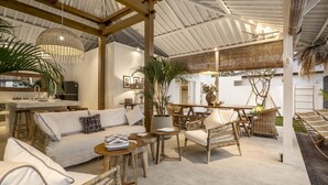 A spacious outdoor lounge area with wicker furniture, a central dining table, and a ceiling with exposed beams. - A Casa Di Renucci by Alfred in Bali (Seminyak)