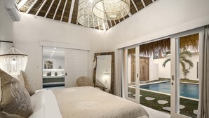 A bedroom with a large bed, a chandelier, and a view of a swimming pool. - A Casa Di Renucci by Alfred in Bali (Seminyak)