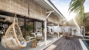 A covered outdoor seating area with wicker furniture, a hanging chair, and a pool. - A Casa Di Renucci by Alfred in Bali (Seminyak)