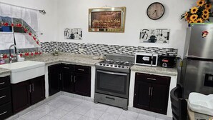 Une cuisine équipée d’un évier, d’une cuisinière, d’un réfrigérateur et d’un four à micro-ondes. Des objets décoratifs ornent le mur, et il y a une horloge.
