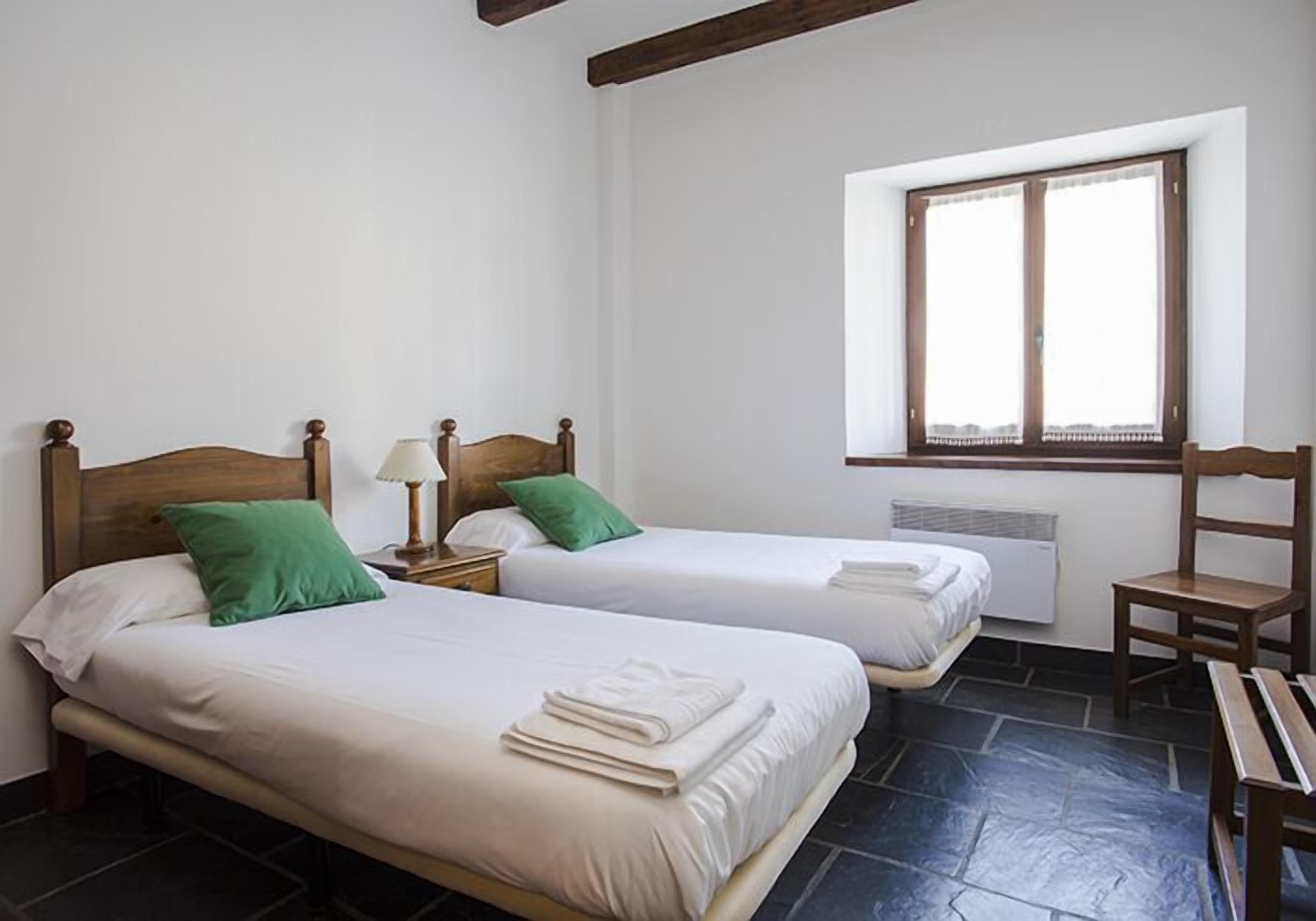 A room with two beds, a window, and a chair.