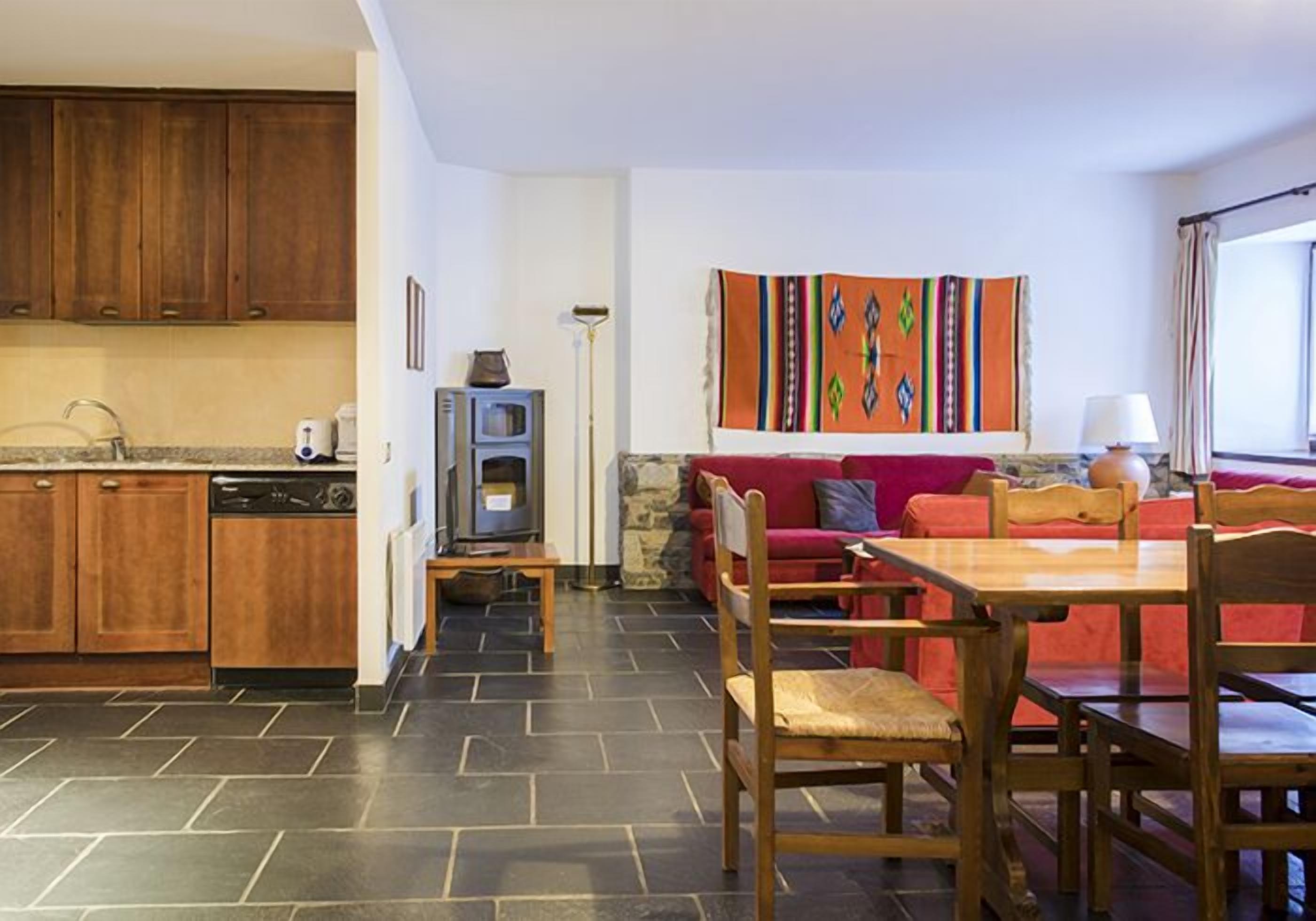 A modern kitchen with dark tiles, wooden cabinets, and a dining area with a red sofa and wooden chairs.