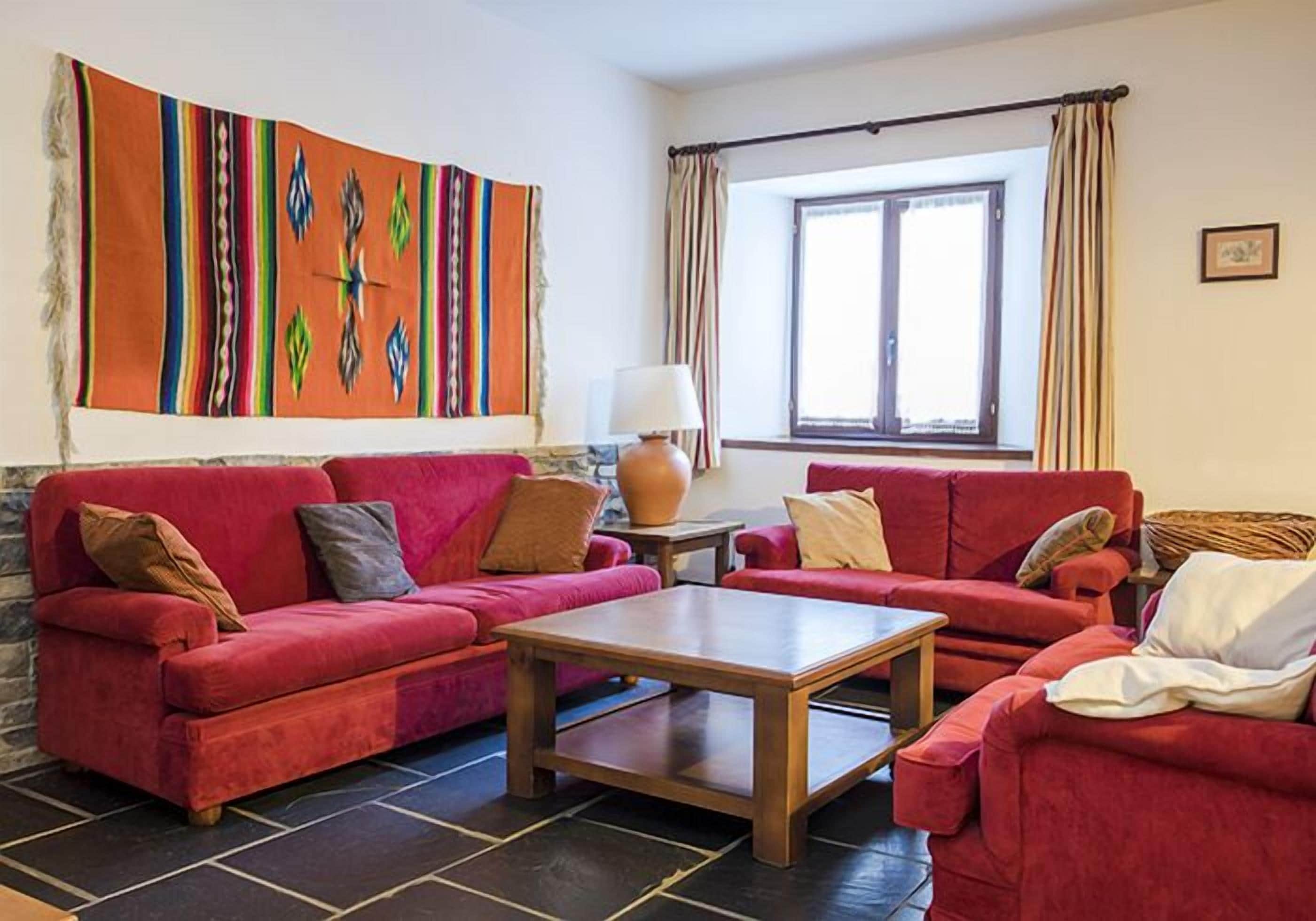 Een woonkamer met rode banken, een houten salontafel en een kleurrijk abstract schilderij aan de muur.