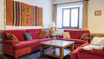 Een woonkamer met rode banken, een houten salontafel en een kleurrijk abstract schilderij aan de muur.