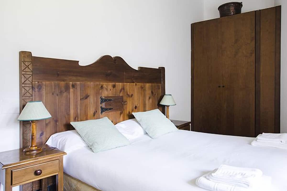 Una cama con cabecera de madera, dos lámparas de noche y una mesita de noche con un cajón.