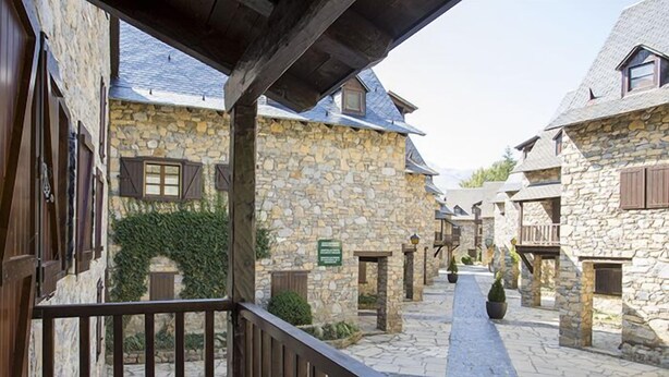 A stone building with a wooden balcony, a stone pathway, and a small garden area. - Apartamentos Linsoles (Benasque)