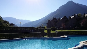A swimming pool with a mountain backdrop, surrounded by well-maintained hedges and traditional buildings. - Apartamentos Linsoles (Benasque)