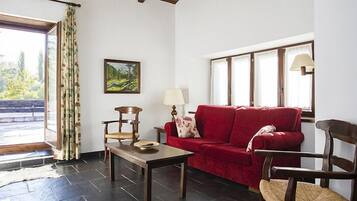 A living room with a red sofa, wooden chairs, a table, and a painting on the wall.