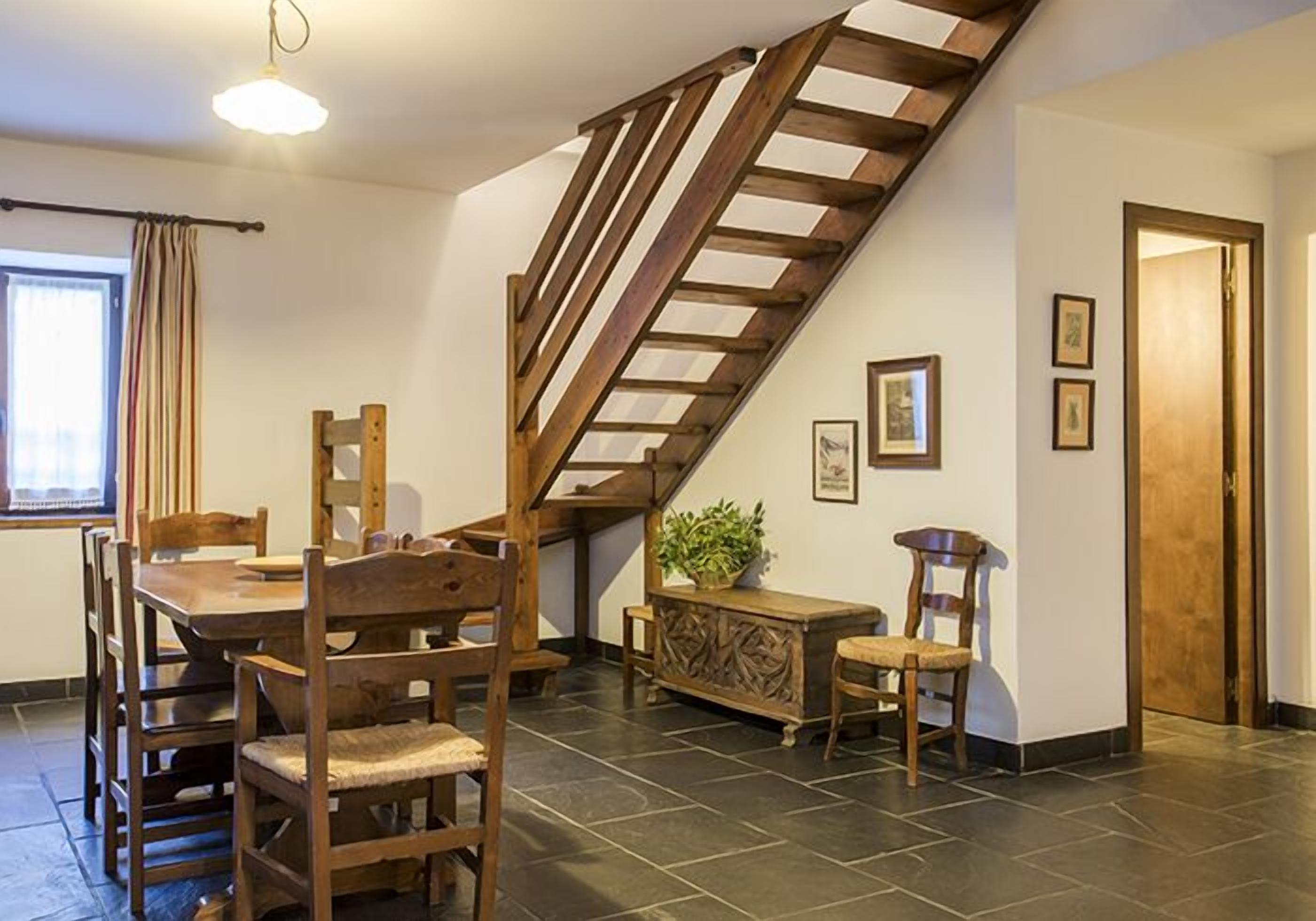 Un coin repas avec un escalier en bois, une table à manger avec des chaises, un buffet et une plante en pot.