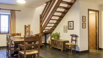 Un coin repas avec un escalier en bois, une table à manger avec des chaises, un buffet et une plante en pot.