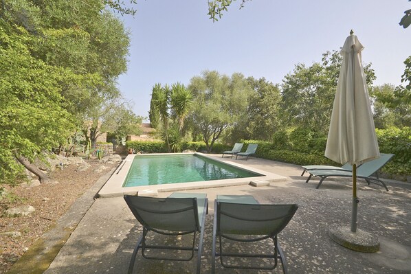 Una piscina rectangular con un patio circundante, que incluye sillas de descanso y una mesa.