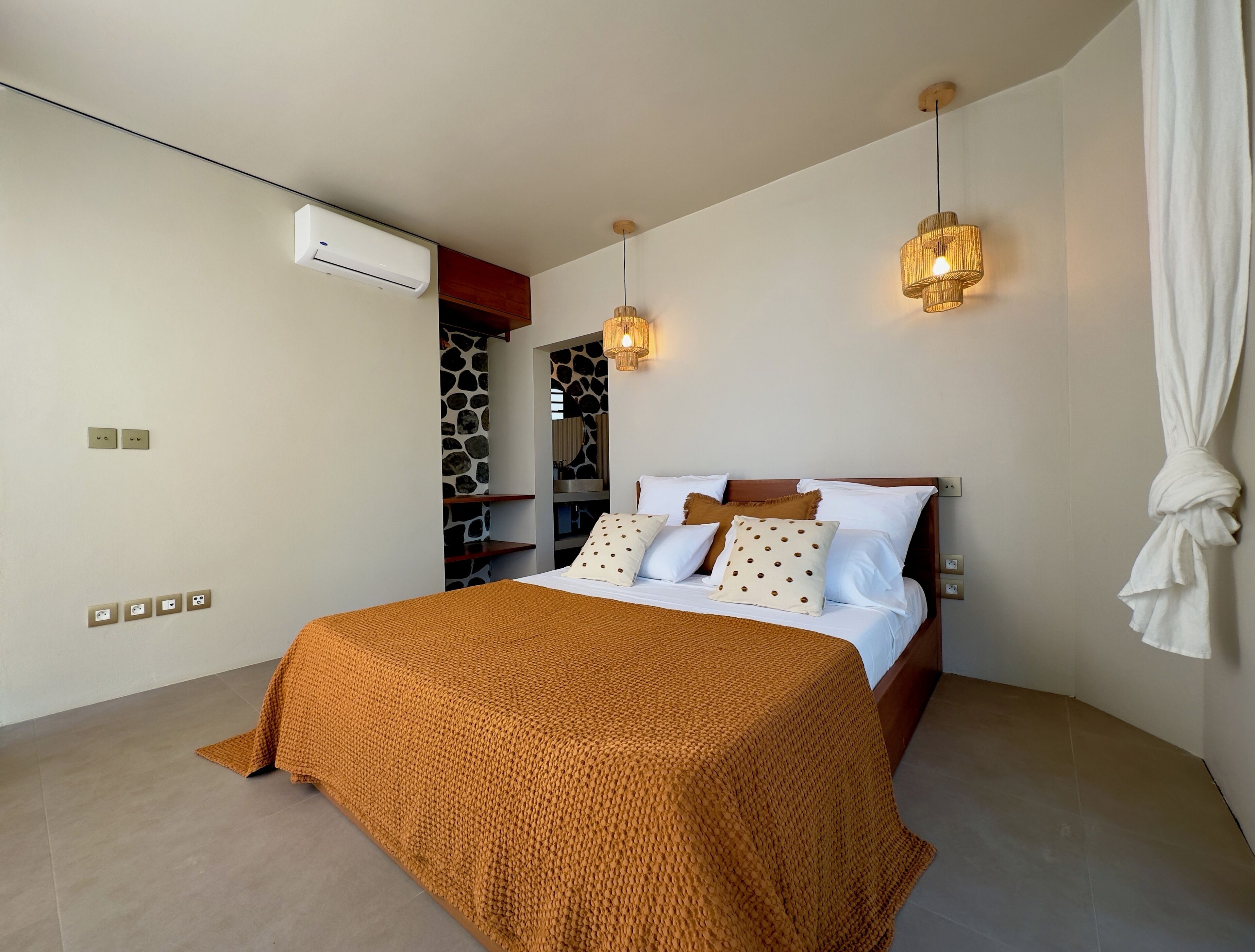 Um quarto moderno com uma cama grande, duas luzes fixadas na parede, uma parede de pedra e uma prateleira embutida.