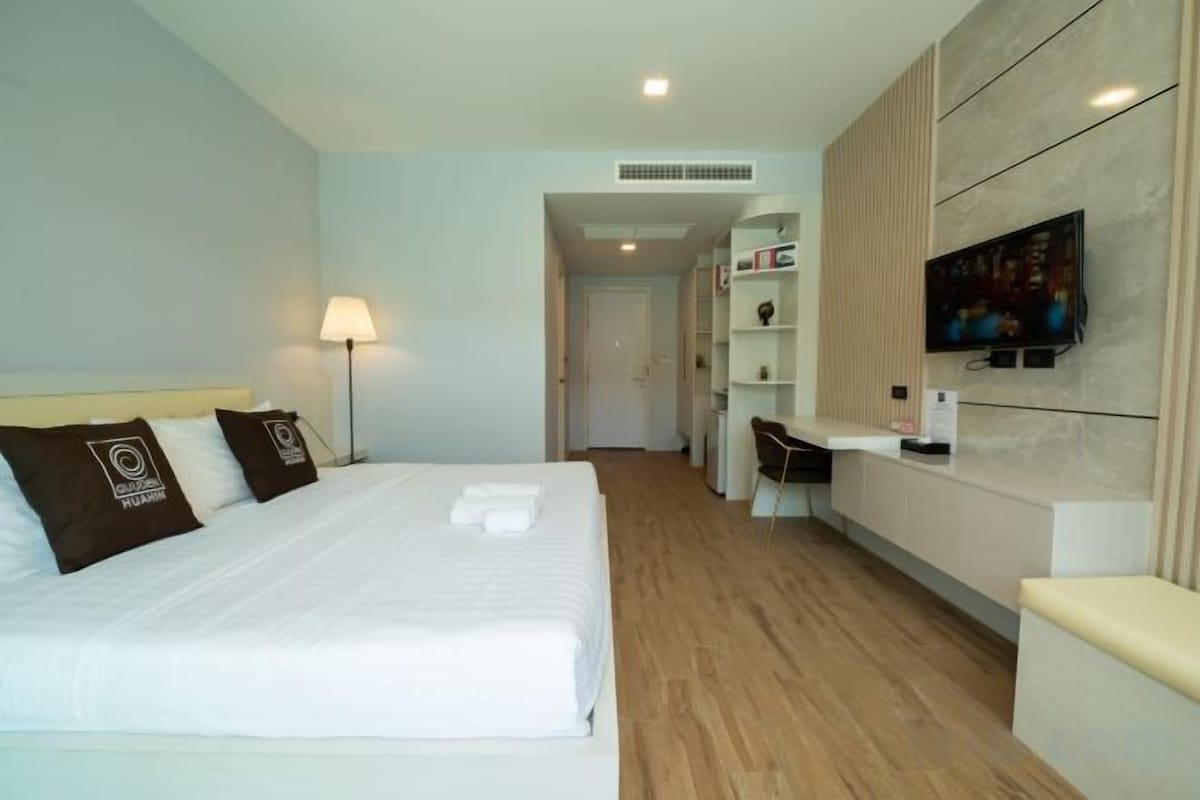 A hotel room with a bed, bedside lamp, TV, and a desk with a chair.
