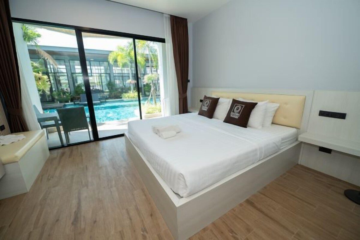 A modern hotel room with a large bed, a small desk, and a view of an outdoor swimming pool.